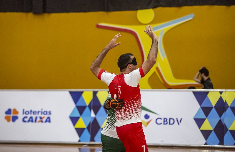 Derocy, de uniforme vermelho, comemora gol abraçado ao goleiro do Escema. Ele ergue os braços e vibra.